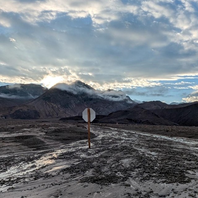 Artists Drive Exit. Sun rising through low clouds hanging over a desert peak.