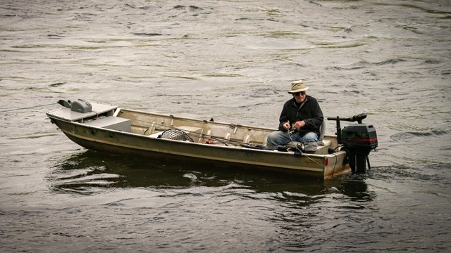 A lone fisherman sits in a small boat fishing the Delaware River.