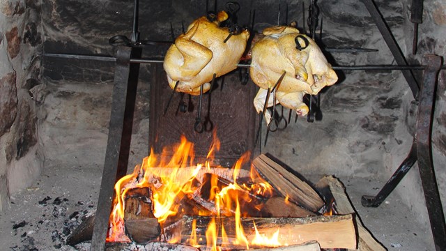 Chickens grilling in a stone fireplace with wood burning gently below