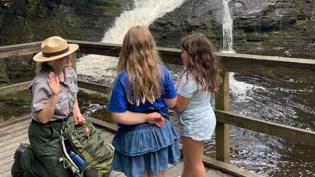 A ranger swearing in two junior rangers in front of Dingmans Falls.