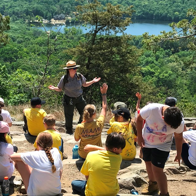 A ranger stands in front of a group of students on a rocky outcropping.