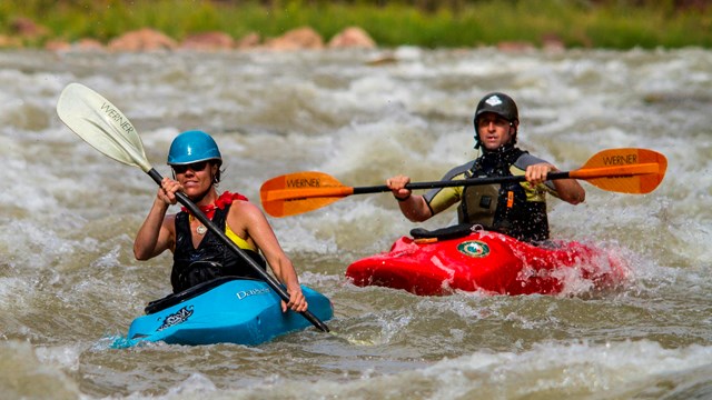 Two kayakers paddling through whitewater on the Green River.