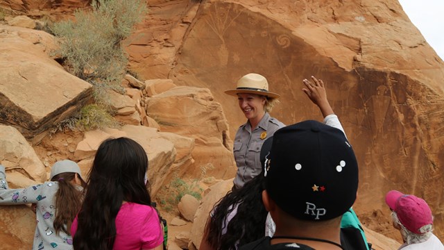 A ranger smiles, surrounded by kids in front of a panel of petroglyphs.