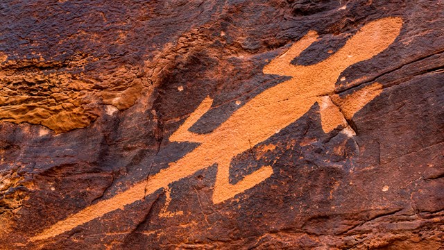 A petroglyph, or rock etching, of a lizard in reddish sandstone.