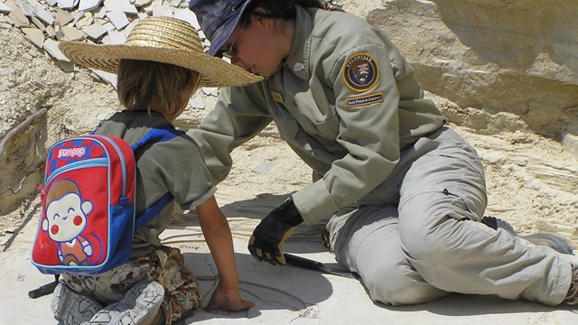 Woman volunteer and child sitting on rock looking at fossils