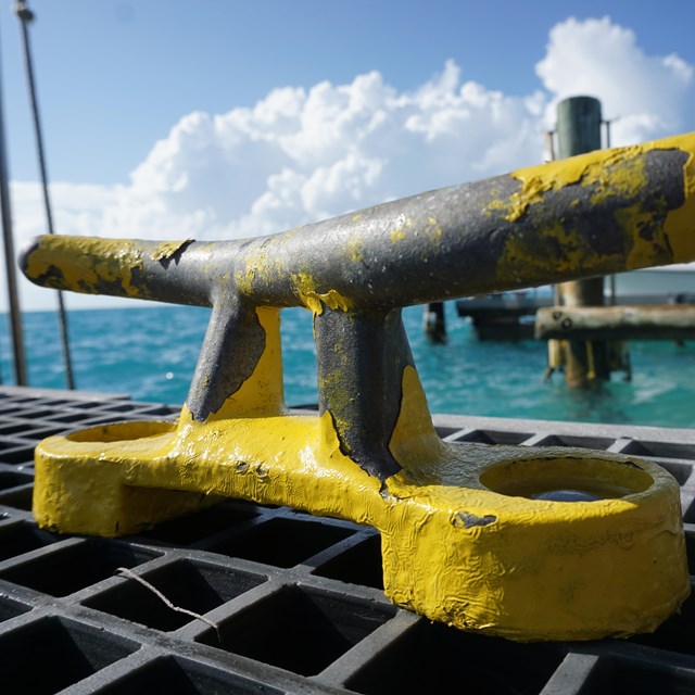 A yellow boat cleat on a pier with blue ocean waters in the background