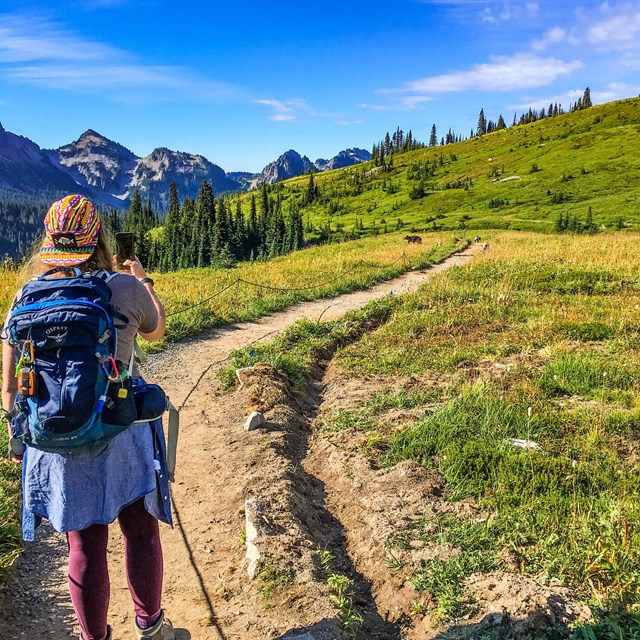 a hiker takes a photo with her phone while hiking on a trail in the mountains