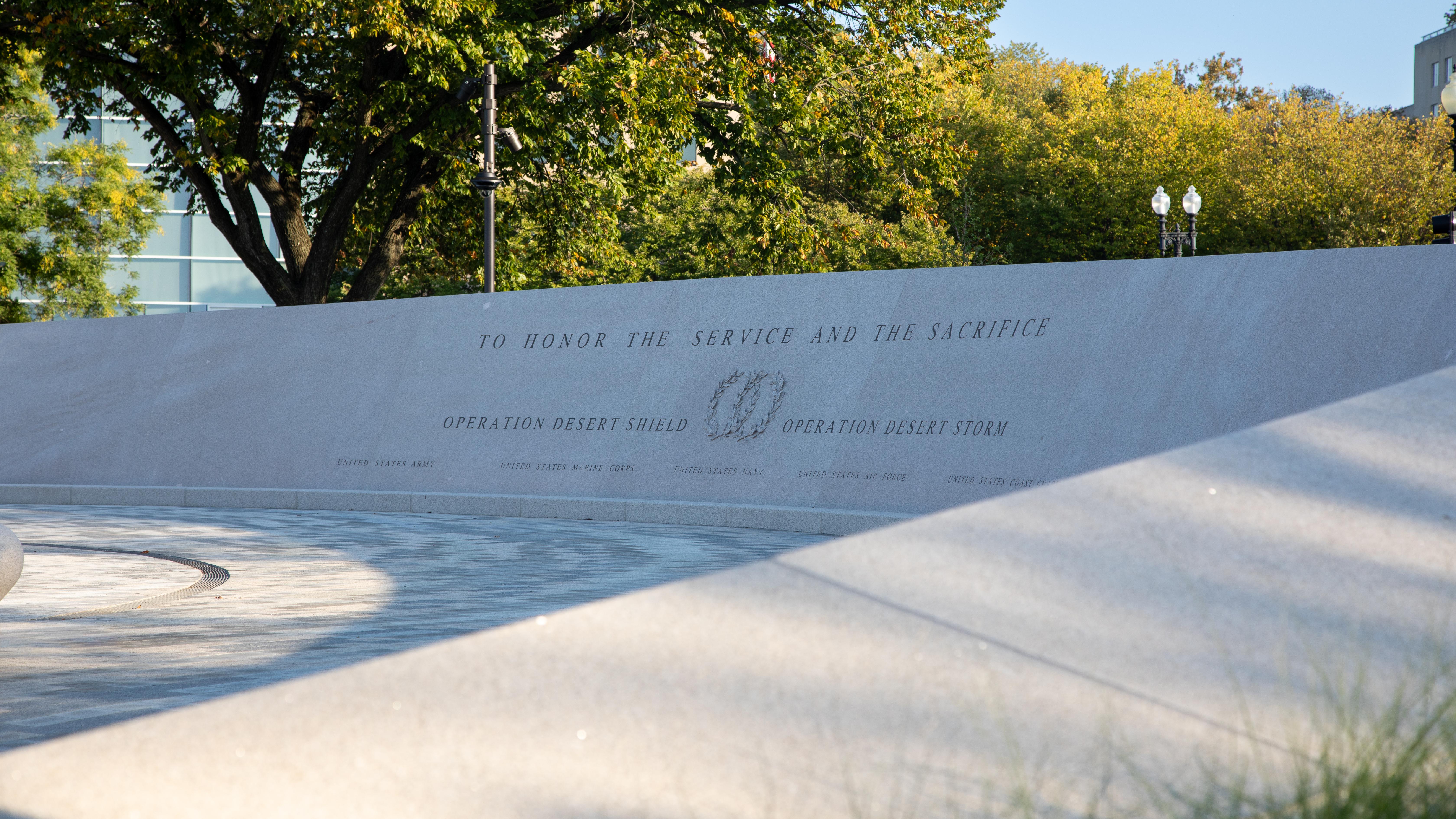A curving wall with inscriptions on it in a shady area.