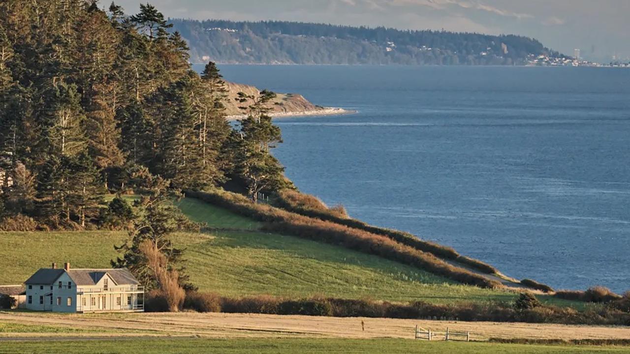 A historic house sits on a grassy prairie near the ocean. 