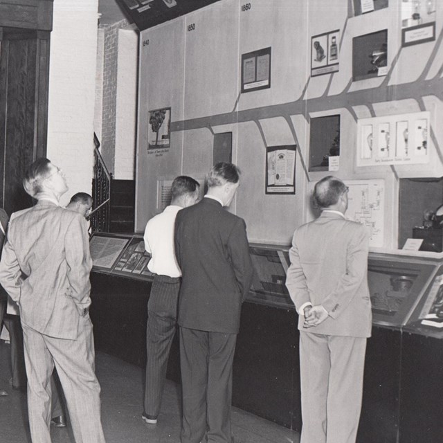 A group of people looking at a timeline of Edison's work (historic exhibit, black and white photo)