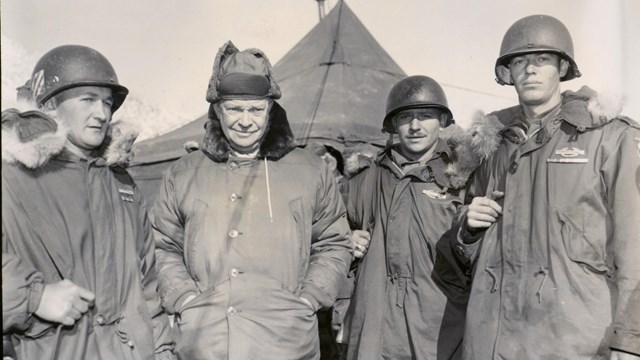 A black and white image of four men standing outside in heavy coats
