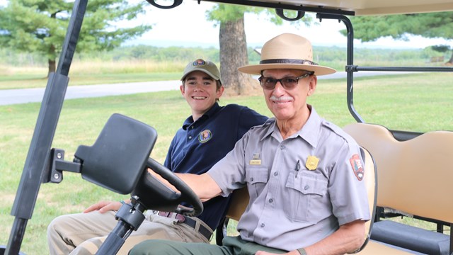 An image of a park ranger and summer intern sitting next to each other on a golf cart