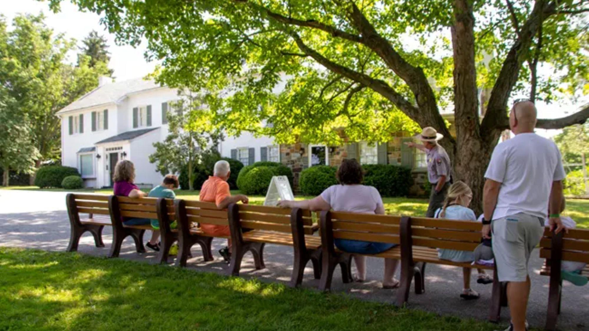 A park ranger and a group in front of the white brick Eisenhower home