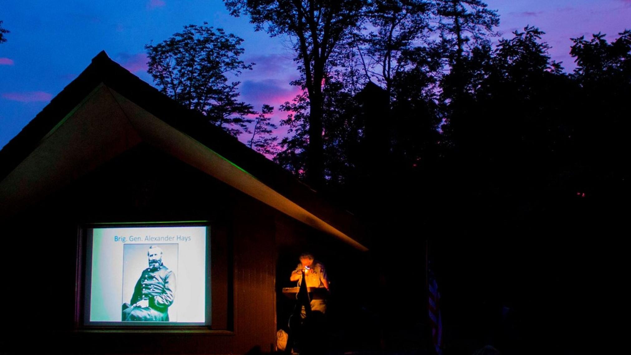 A park ranger speaks at a podium on an amphitheater stage at nighttime
