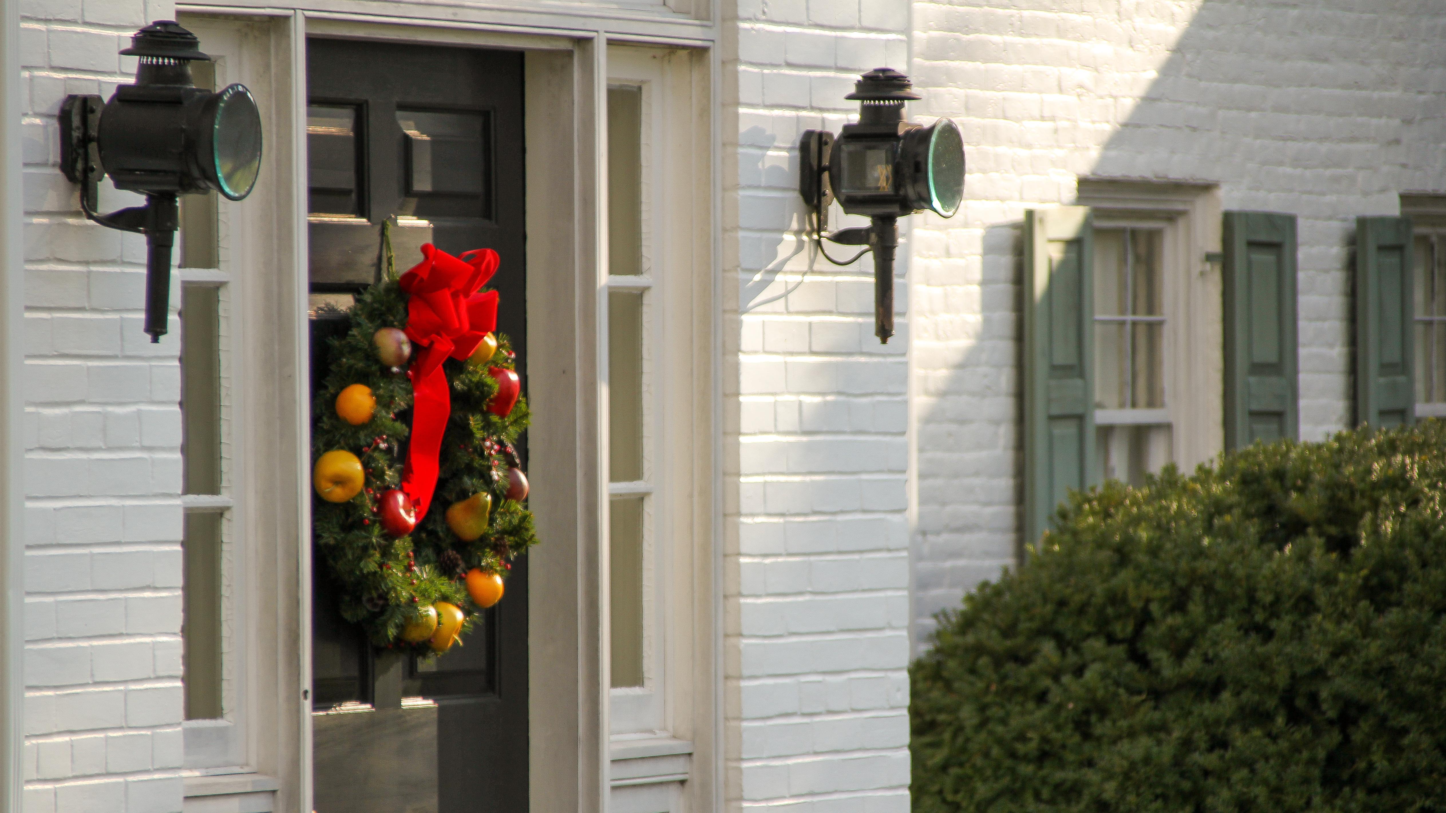 A colorful wreath hangs on the black front door of a white brick home