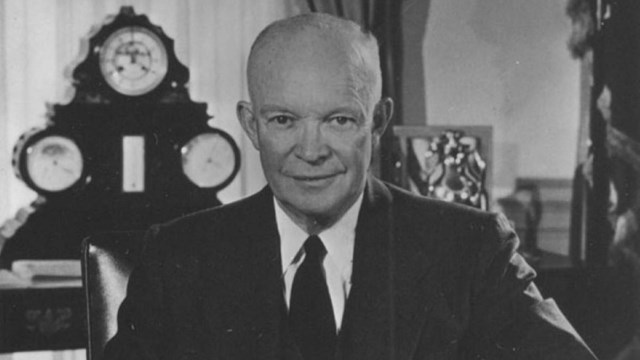 A black and white picture of a man in a suit sitting at a desk