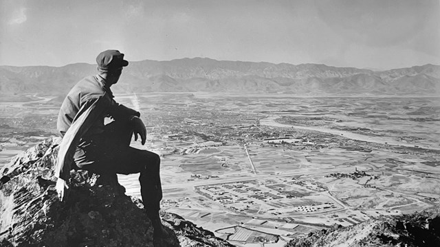 A black and white image of a man on a mountain looking out across the Korean countryside