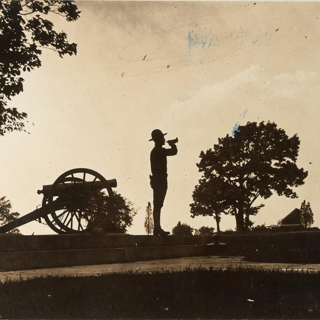 A silhouette of a bugler standing next to monuments and trees