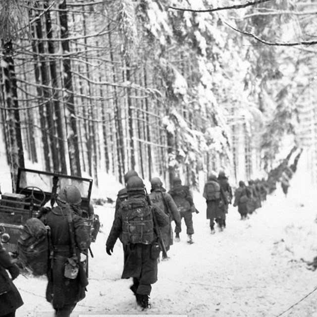 A black and white image of soldiers marching through snow covered woods