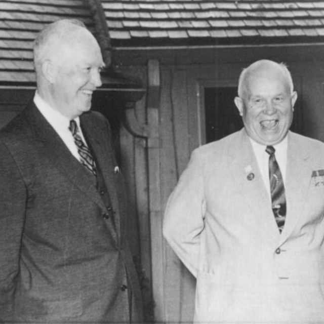 A black and white image of two men standing side by side, both wearing suits