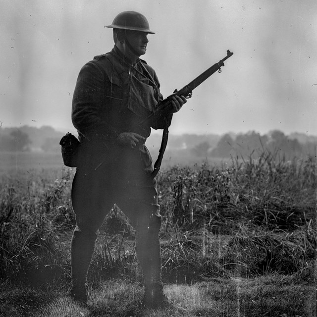 A black and white image of a man wearing an American soldier uniform and holding a WWI era rifle