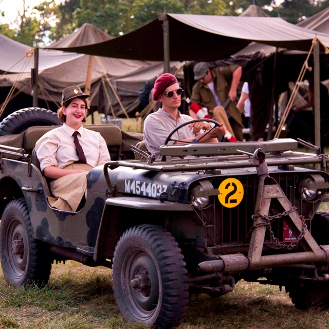 A WWII era Jeep is driven around the park by a re-enactor dressed in military uniform.