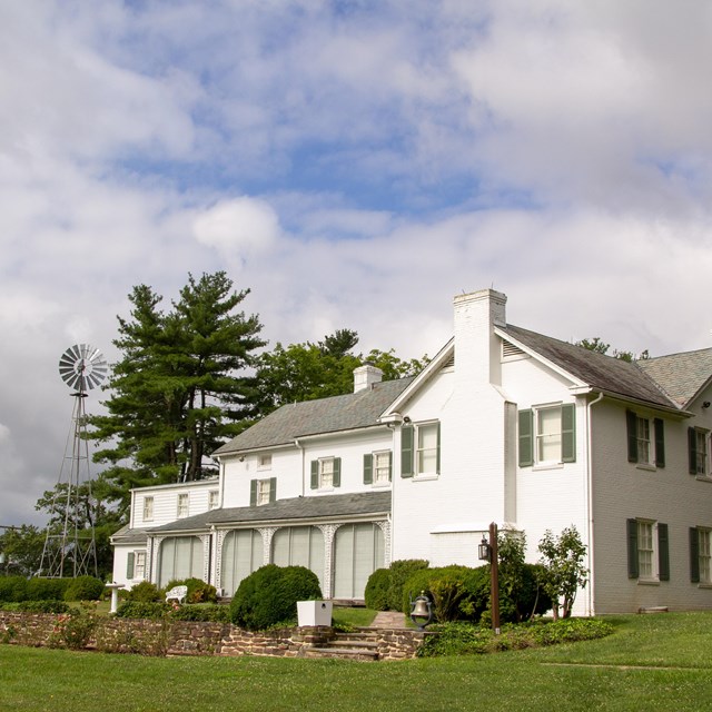 A color image showing the white Eisenhower home with green grass, green trees, and a blue sky