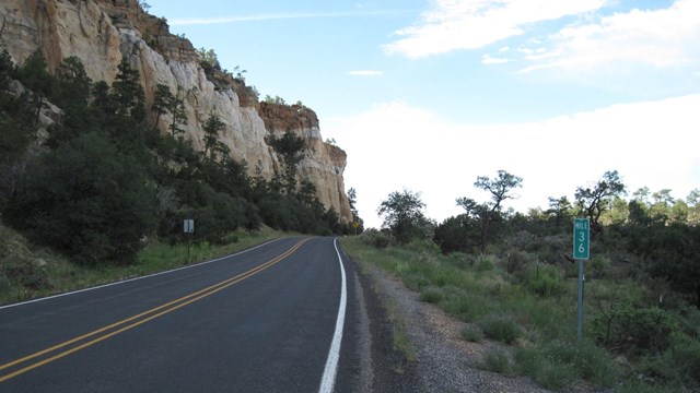 A highway goes between dark lava rock and sandstone cliffs. 