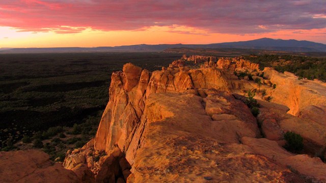 The sunset casts orange and pink light on sandstone cliffs. 