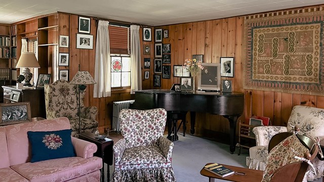 A paneled living room with a piano and many photos on the walls.