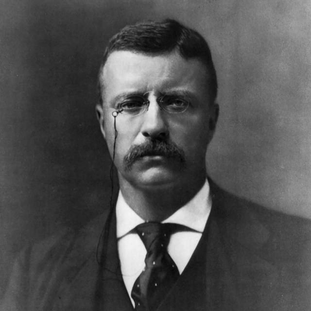 A man in a dark suit wearing glasses.