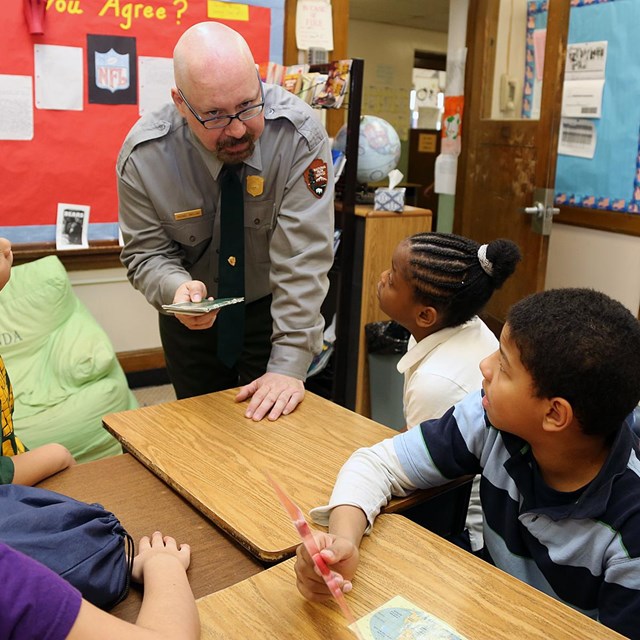 A park ranger stands in a classroom talking to kids at their desks