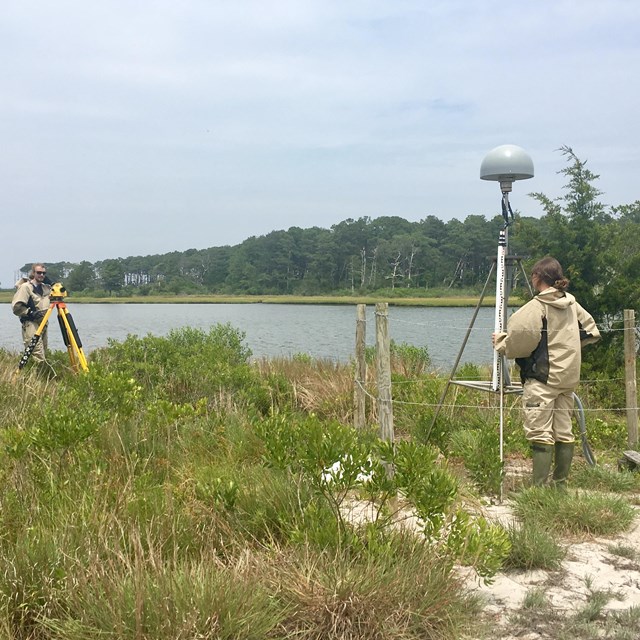 two people operating surveying equipment near a shoreline