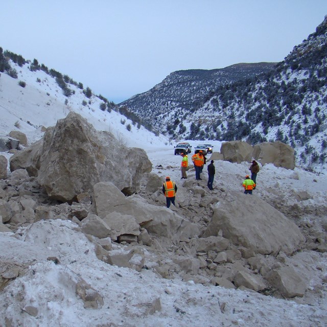 group of people examining a rockfall deposit that has closed the highway