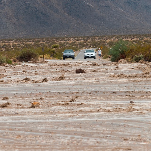  El agua y las rocas inundan una carretera principal con dos vehículos atrapados al otro lado.