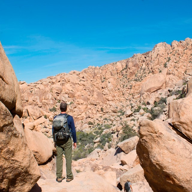  Un hombre se para sobre una pila de rocas, rodeado de grandes montañas de rocas en todas las direcc