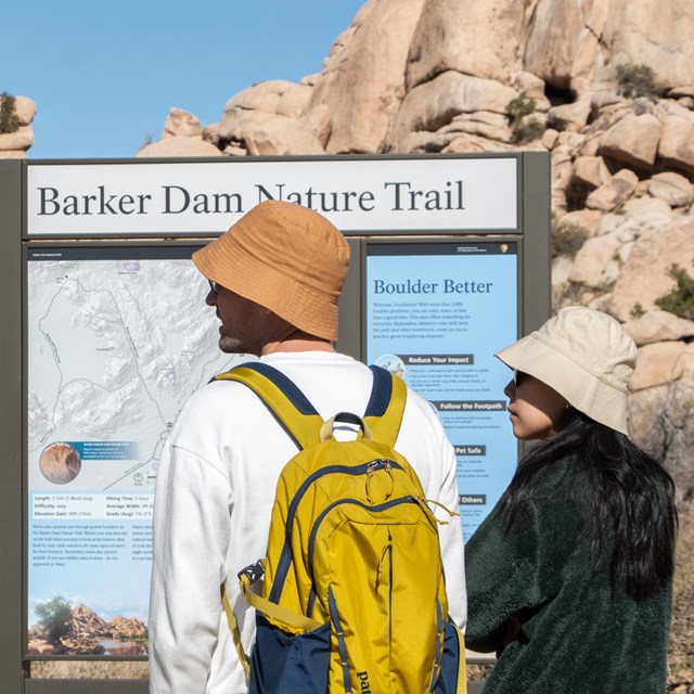 Dos visitantes del parque frente al tablero informativo en la entrada del sendero de Barker Dam.