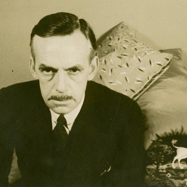 An older man in a suit and tie is posing for the camera. He is not smiling. 