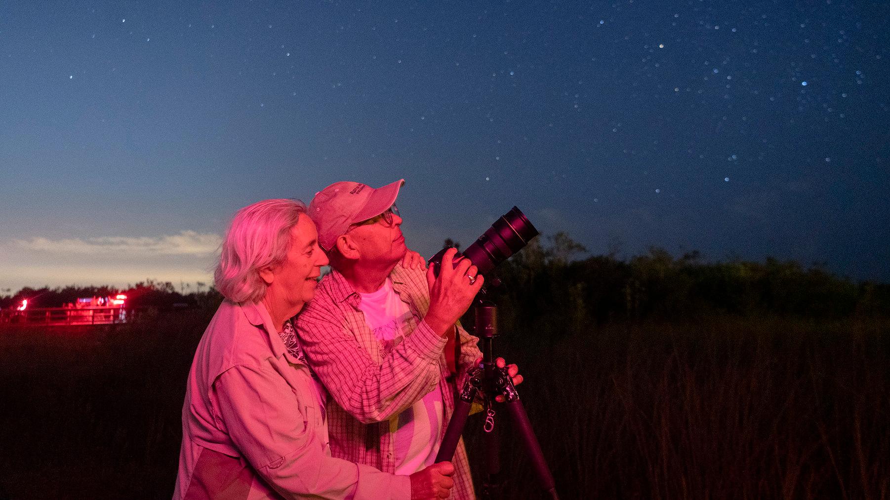 Two people stand by a camera pointed up at a dark night sky.