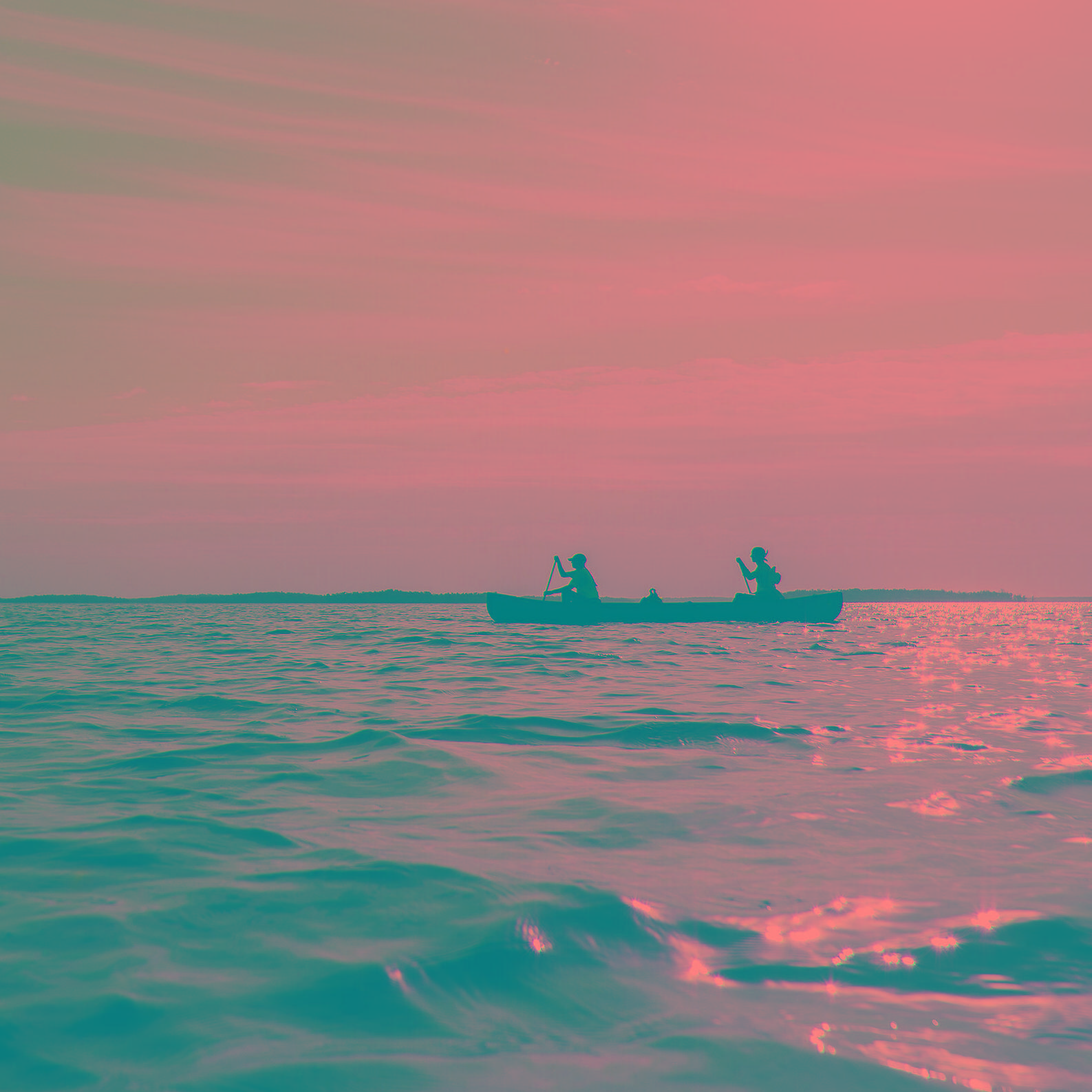 Two people paddle in the distance near islands under a bright sky with wispy clouds.