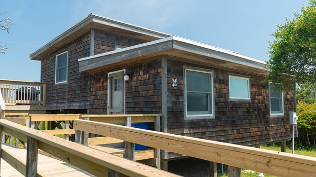 A split level square beach house with wooden siding.