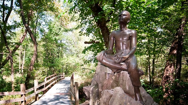 Bronze statue of boy sitting on rock gazing up