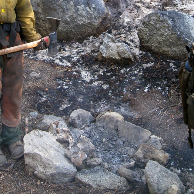 A firefighter stands next to the point of origin of an escaped campfire.