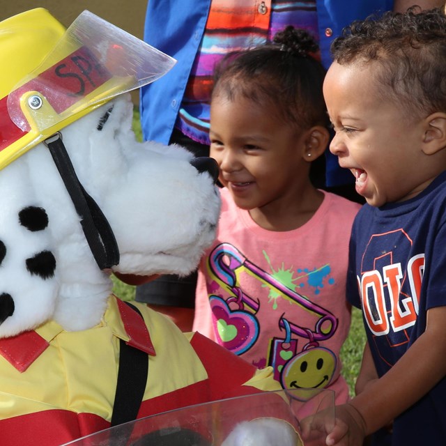 Two children laugh with Sparky the Fire Dog.