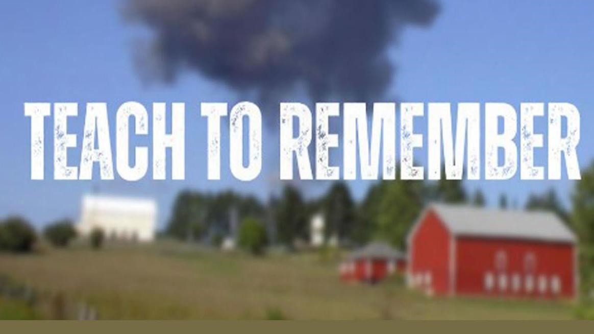 A large black smoke plume behind a red barn and a rural landscape