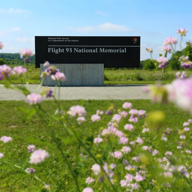 The Flight 93 National Memorial entrance sign surrounded by wildflowers and green grass.