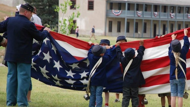 Image of rangers and kids dressed as 1870 soldiers folding the American Flag. 