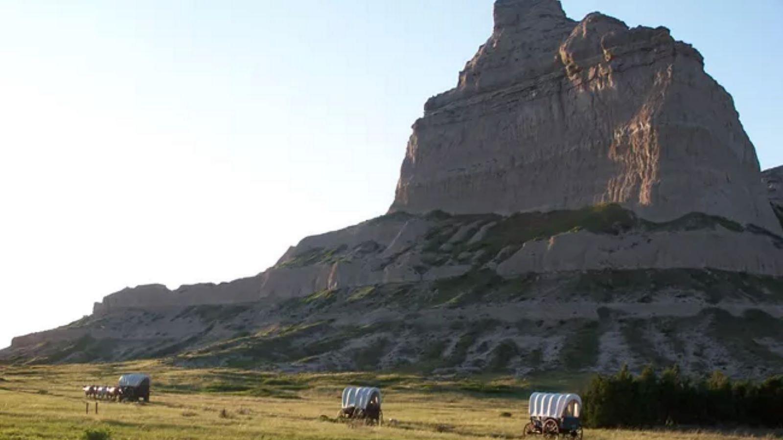 Image of Eagle Rock with three covered wagons underneath it. 