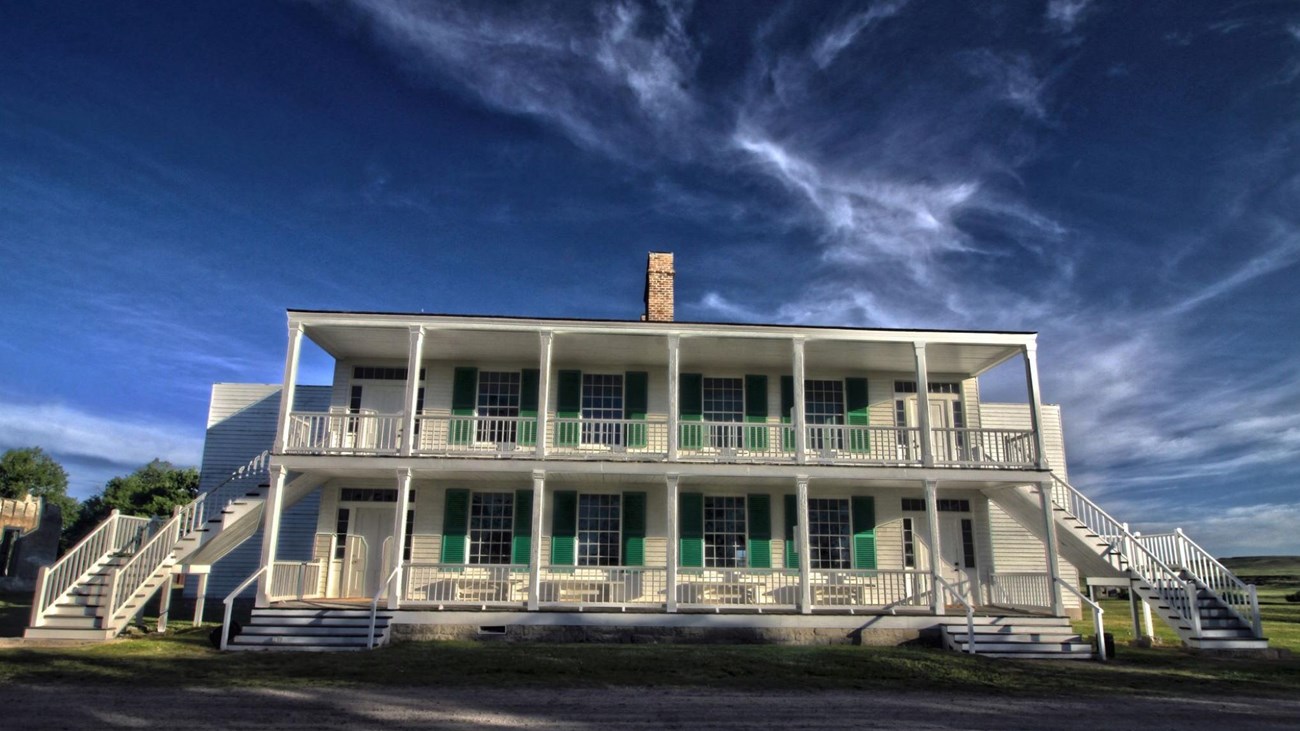 Image of large white building with a wraparound porch and green doors. 