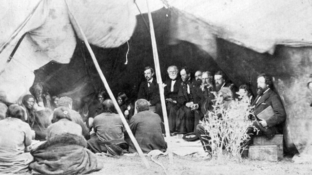 Image of seven officers in coats meeting with several American Indian men. 